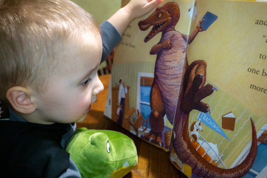 Preschooler with toy dinosaur reading a dinosaur book for kids